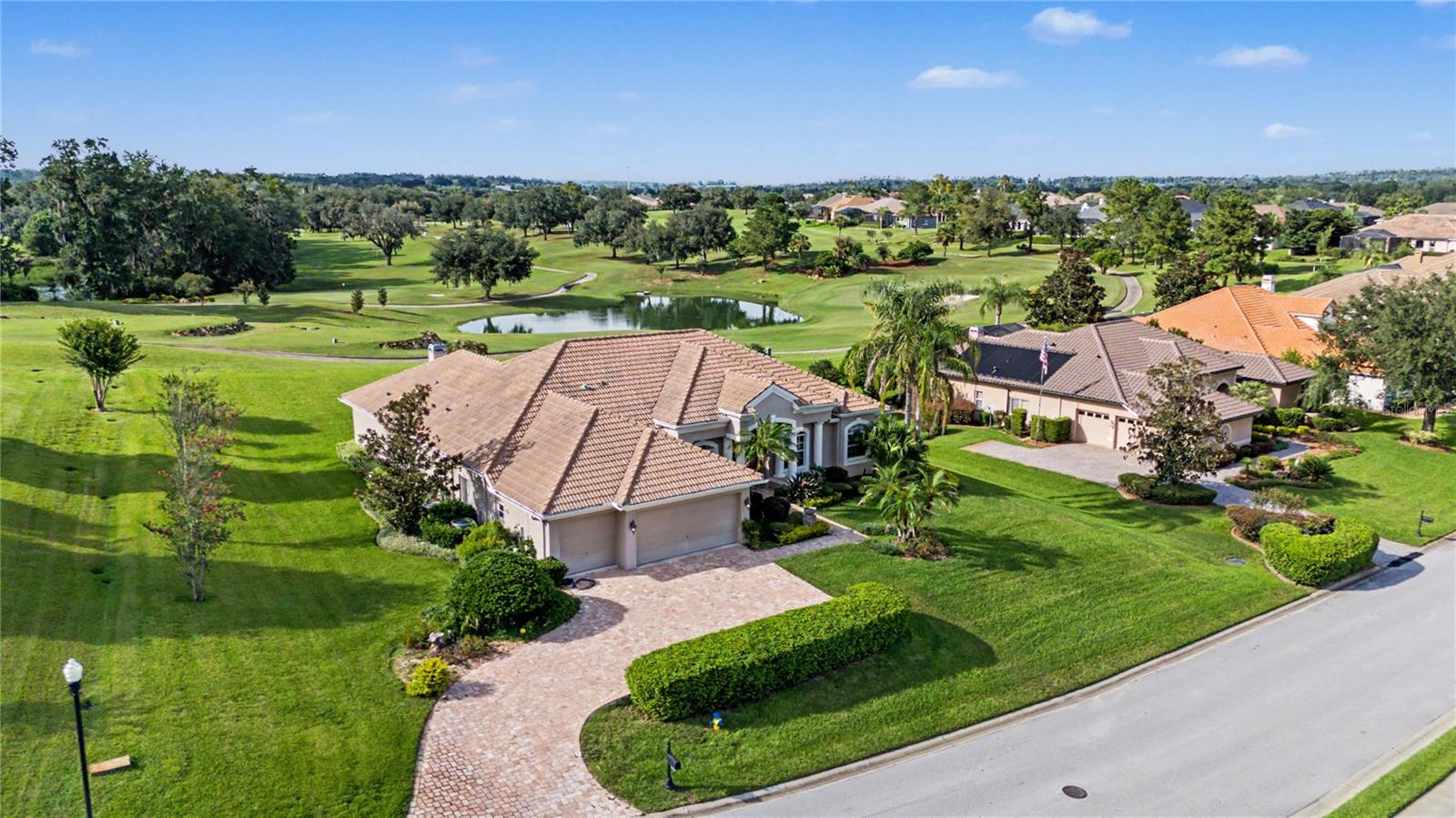 Aerial view of a tiled-roof home beside a golf course and pond.