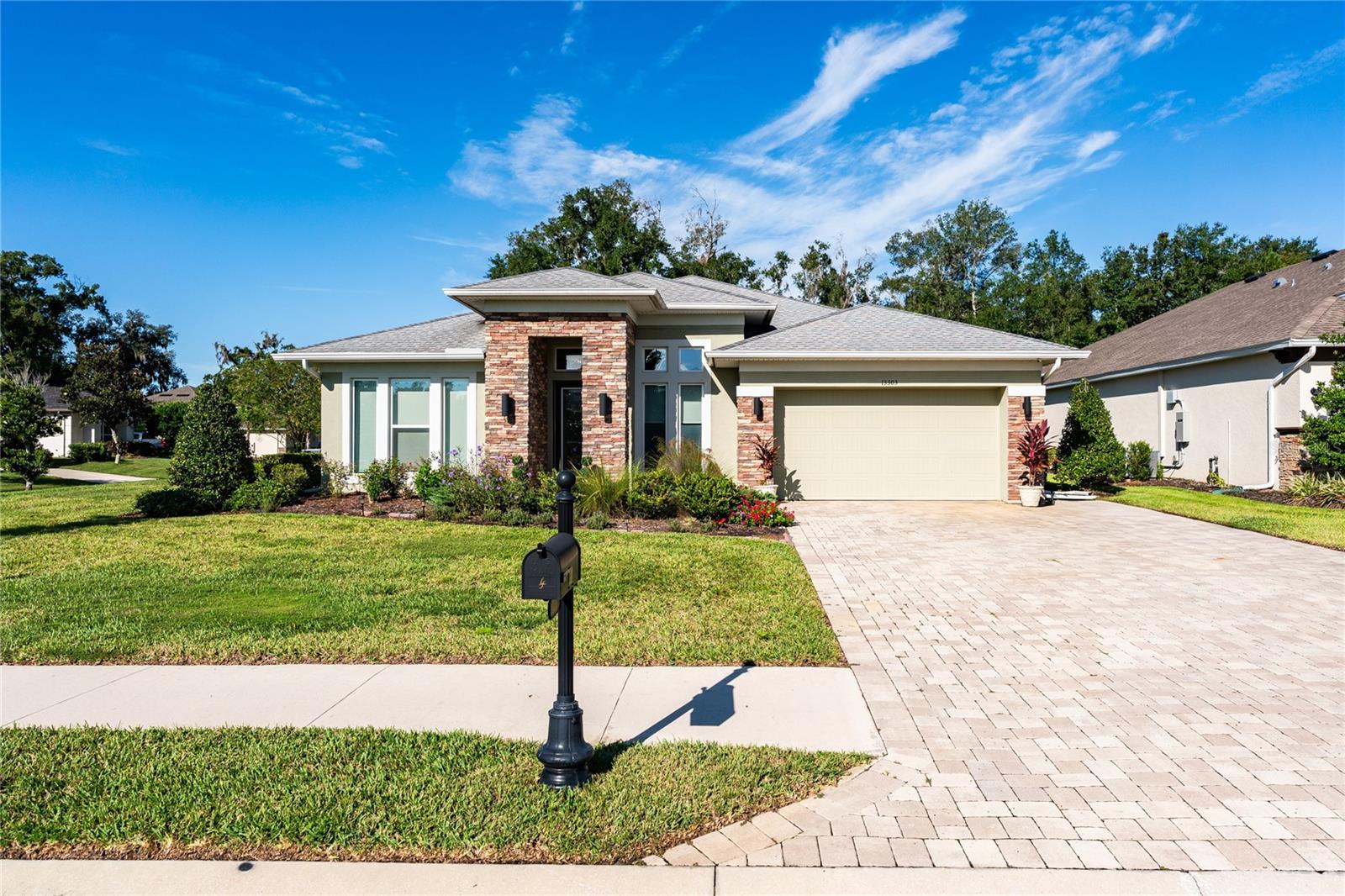 Modern single-story home with a stone entry, landscaped lawn, and paver driveway.