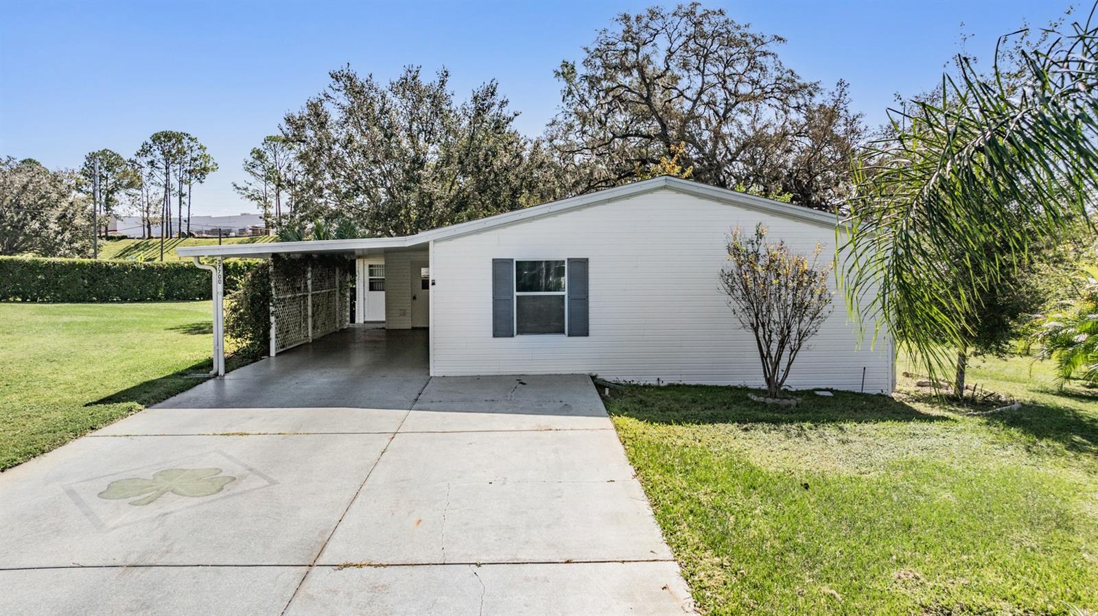 White single-story home with a covered carport, blue-gray shutters, and a broad concrete driveway.