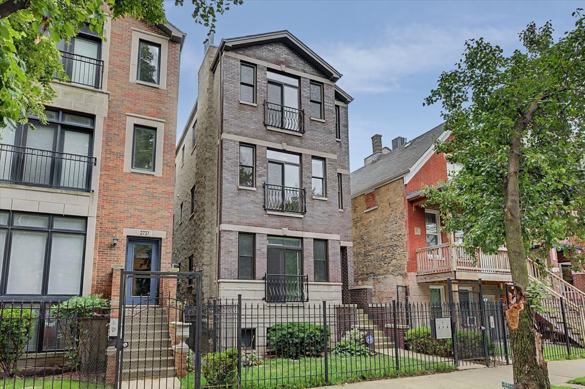 Gray brick multi-unit residence with small balconies behind a black iron fence.