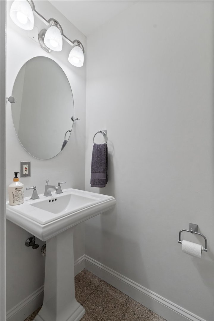 Bathroom pedestal sink with an oval mirror, three-light fixture, and gray towel.