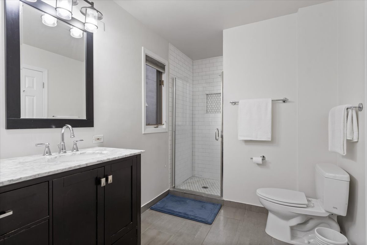 Bathroom with a dark marble-topped vanity and glass-enclosed subway-tile shower.