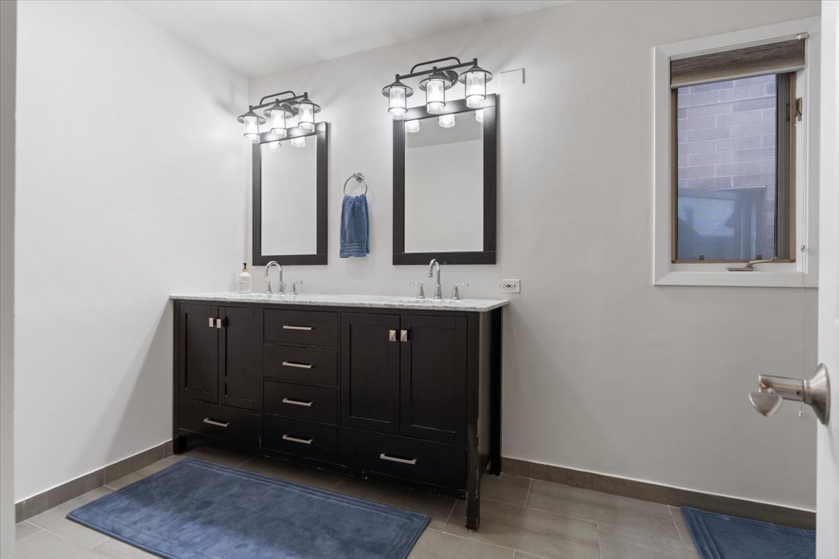 Bathroom with a dark double vanity, two mirrors, and a window.