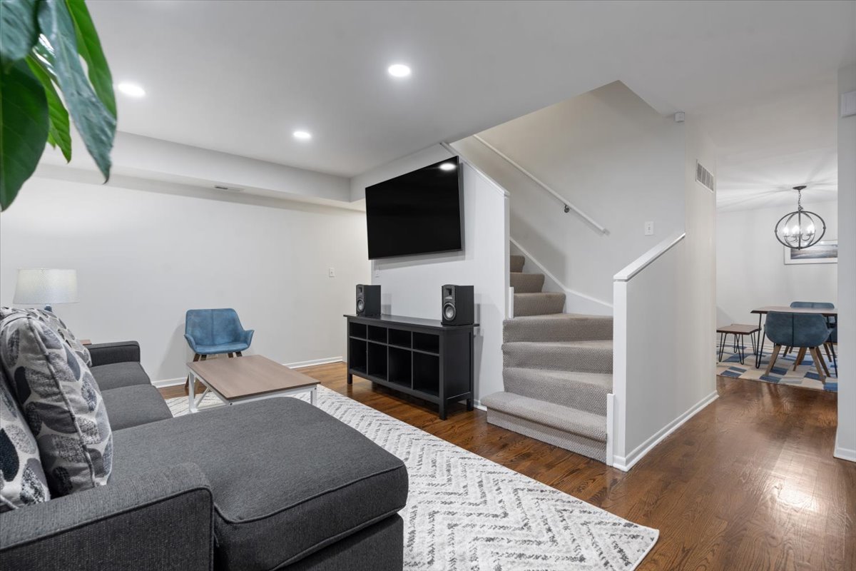 Living room with a gray sectional, wall-mounted TV, and staircase beside the dining area.