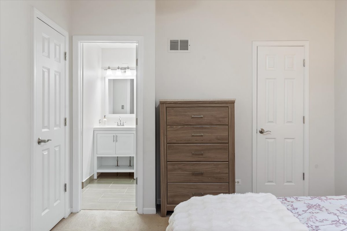 Bedroom with a wood-tone chest of drawers and an open doorway to a bathroom vanity.