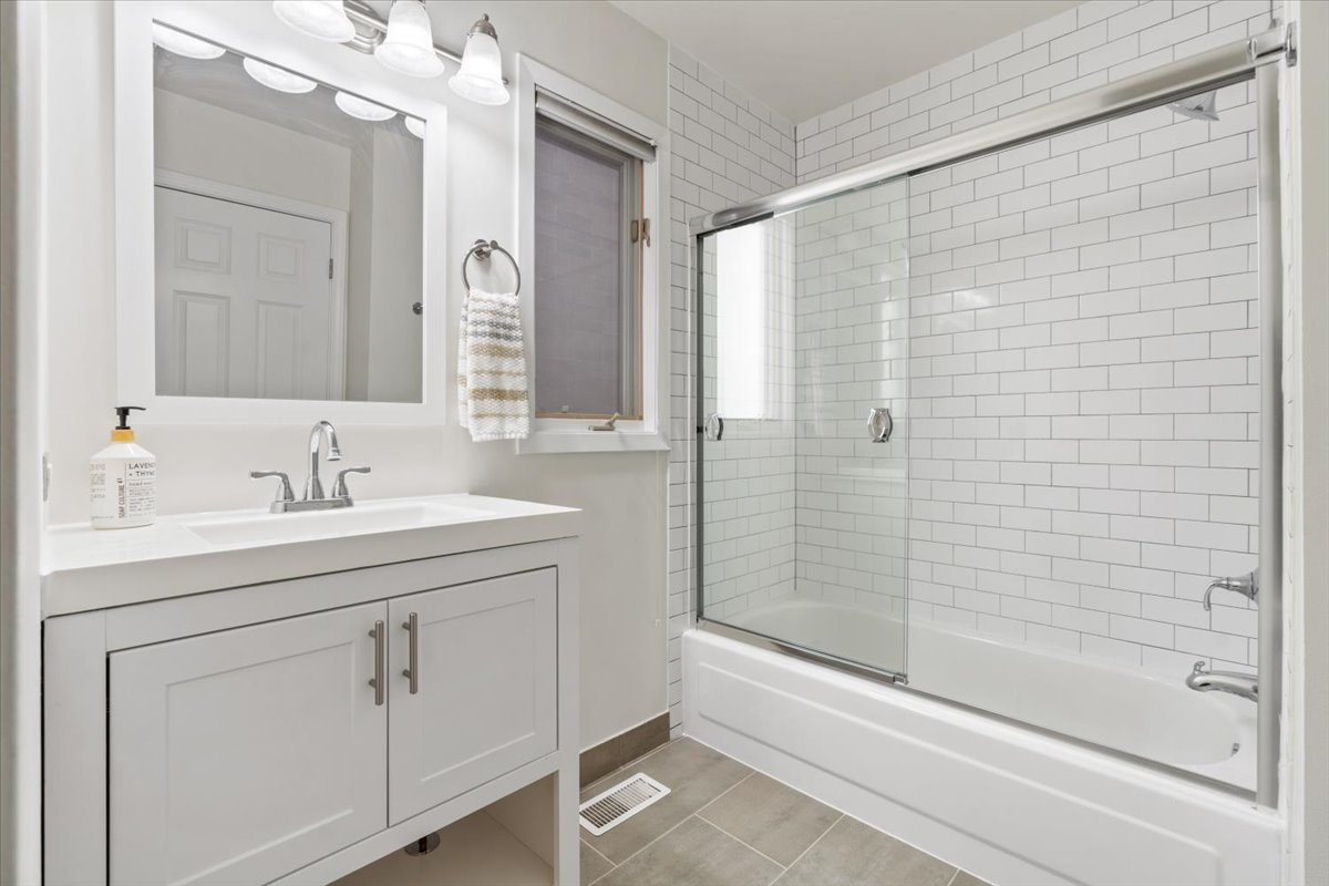 Bathroom with a white vanity and mirror beside a subway-tile tub and glass shower screen.
