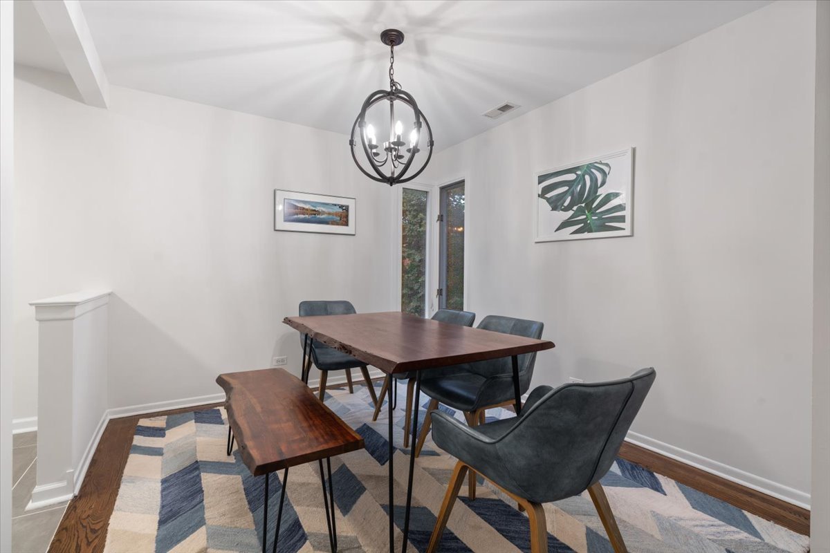 Furnished dining room with a wood table, gray chairs, geometric rug, and chandelier.