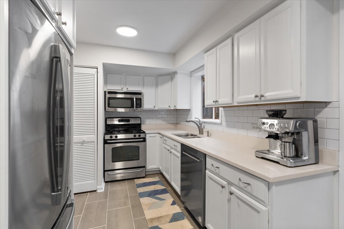 Kitchen with white cabinets, stainless steel appliances, subway tile backsplash, and a patterned runner rug.