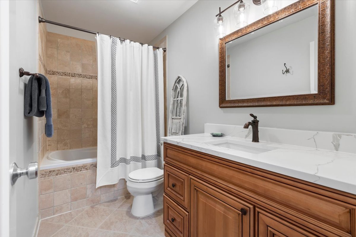 Bathroom with a wood vanity, framed mirror, and tiled tub-shower behind a white curtain.