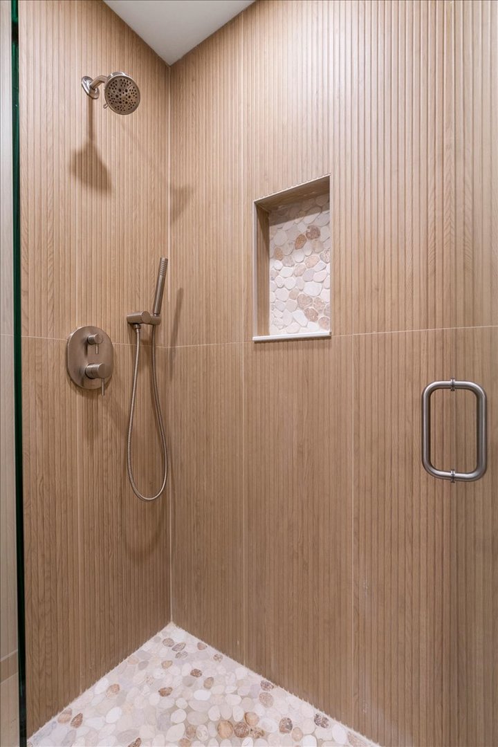 Walk-in shower with vertical wood-look tile, a pebble-lined niche, and handheld shower fixtures.