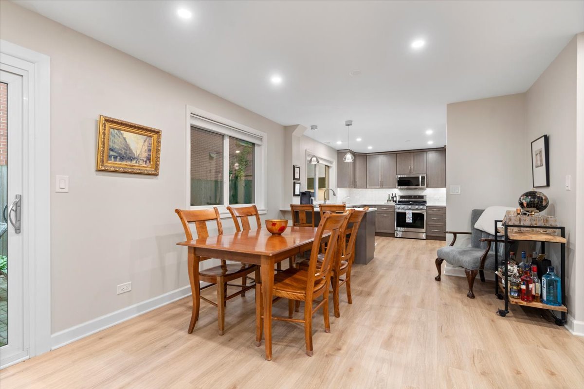 Dining area with a wooden table and chairs opening onto a gray-cabinet kitchen.