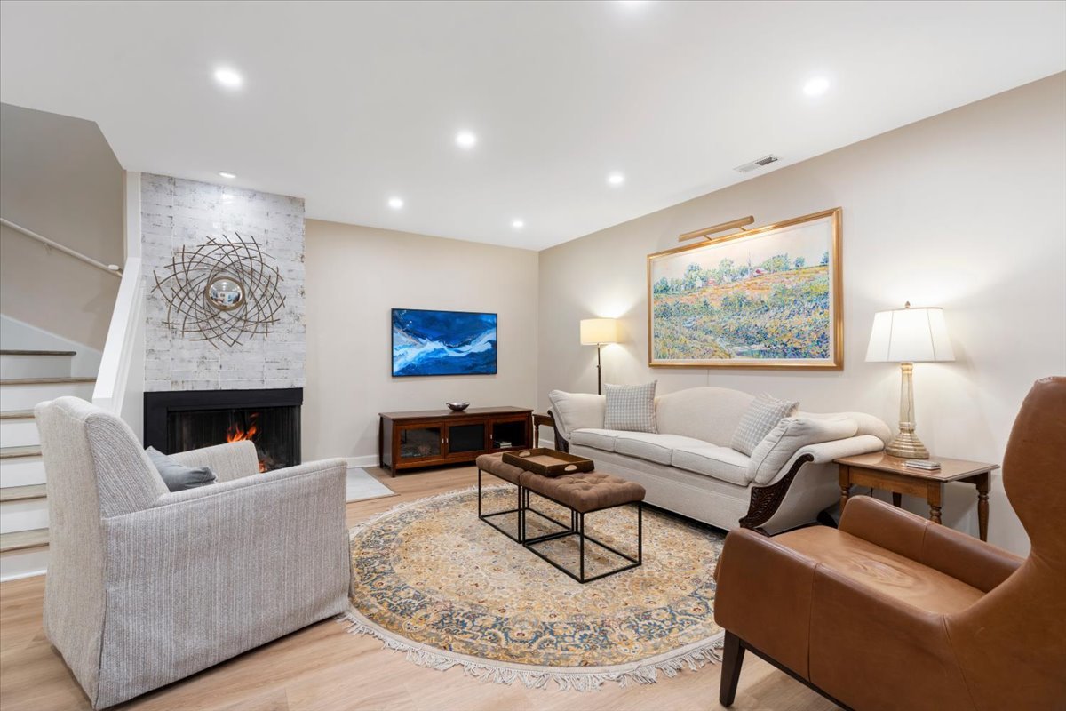 Living room with a lit fireplace, white sofa, patterned rug, and staircase.