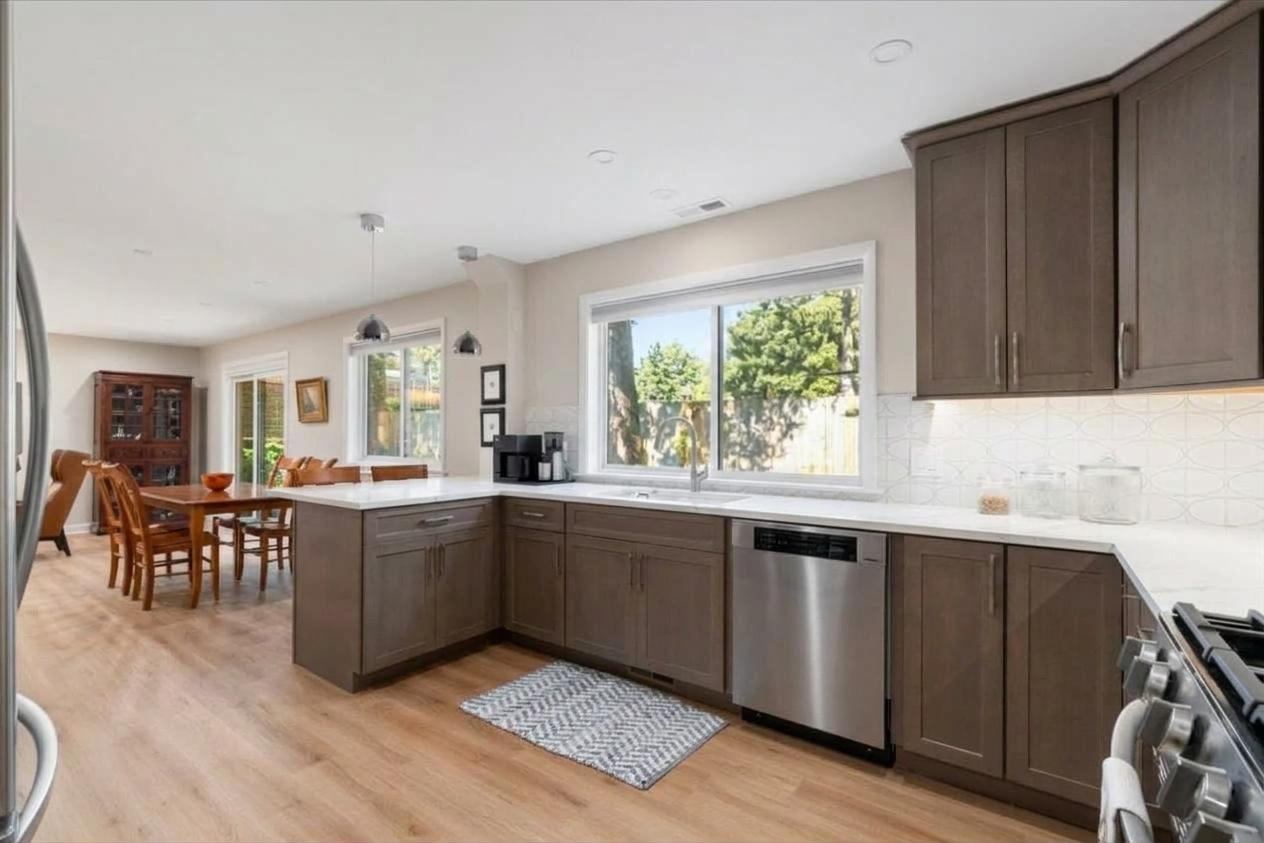 Kitchen with dark wood cabinets, white counters, stainless steel appliances, and windows overlooking a fenced yard.