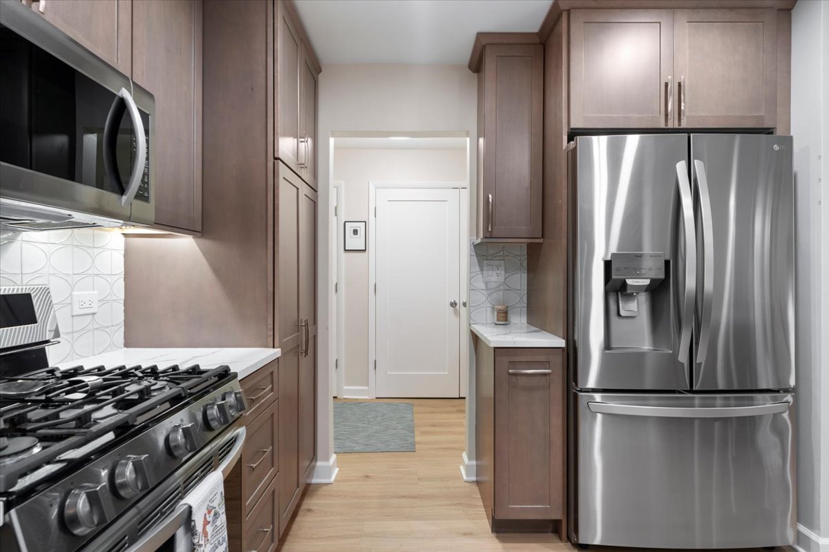 Kitchen with dark wood cabinets, stainless steel appliances, patterned tile backsplash, and light wood flooring.