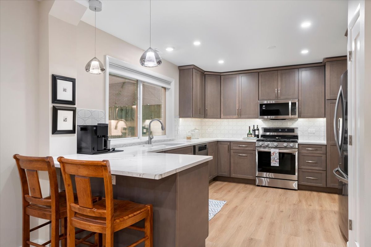 Modern kitchen with a marble island, dark wood cabinets, stainless steel appliances, and two wooden stools.