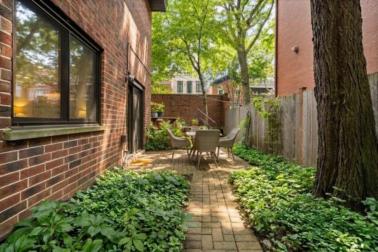 Brick courtyard patio with outdoor dining furniture, mature trees, and leafy garden beds.