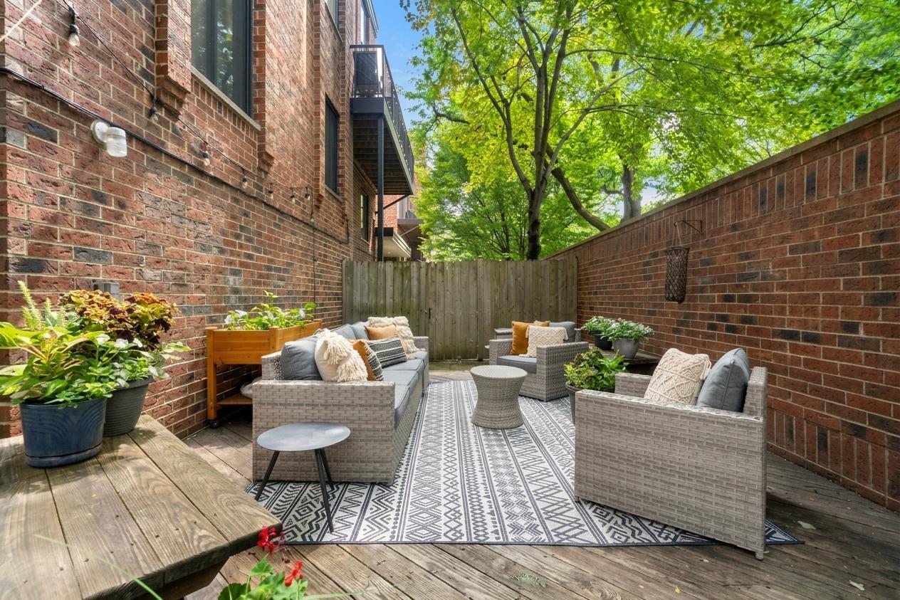 Furnished brick-enclosed patio with wicker seating, a patterned rug, and leafy trees overhead.