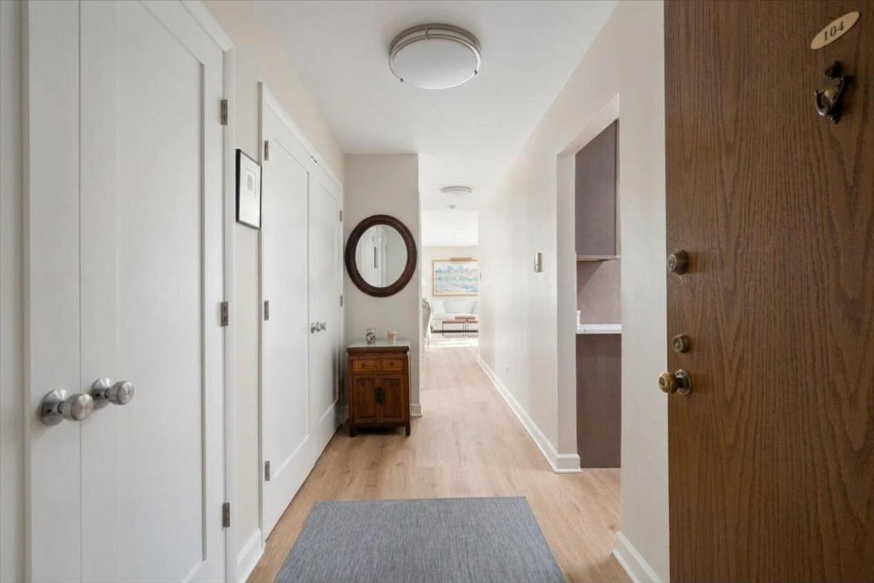 Condominium entry hallway with light wood floors, a gray runner, and a console beneath a round mirror.