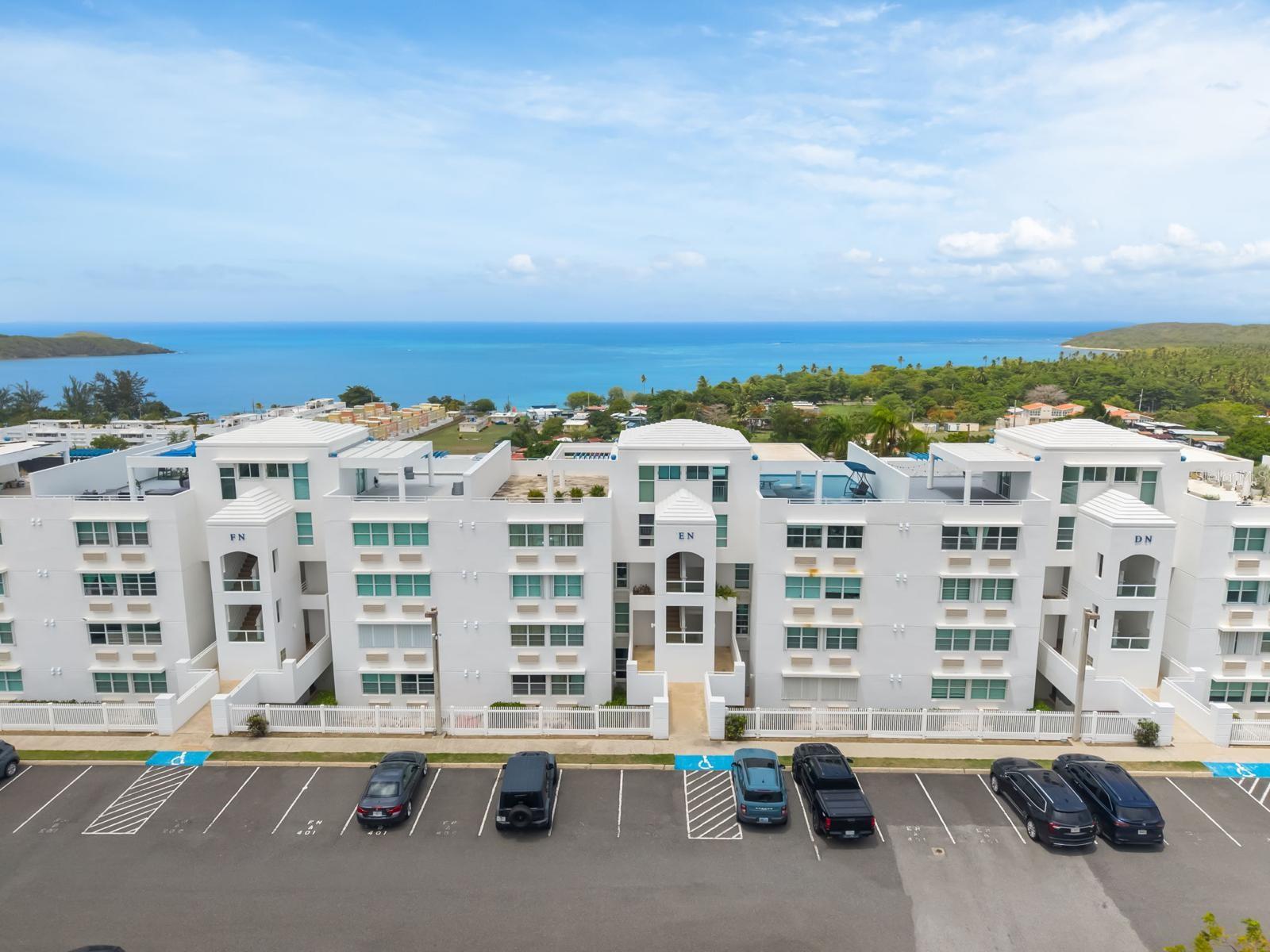 White condominium complex overlooking turquoise ocean, with a coastal shoreline in the distance.