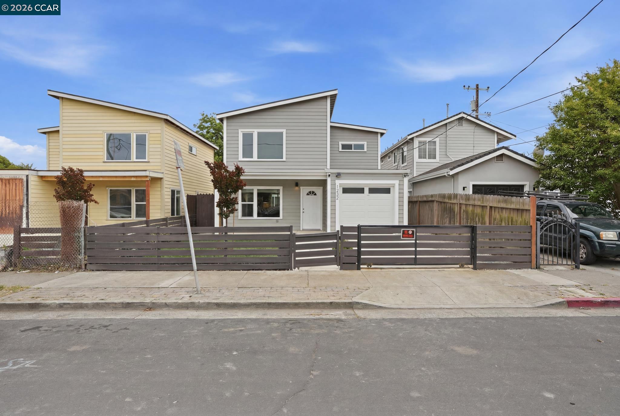 Two-story gray house with an asymmetrical roof and dark horizontal-slat front fence.