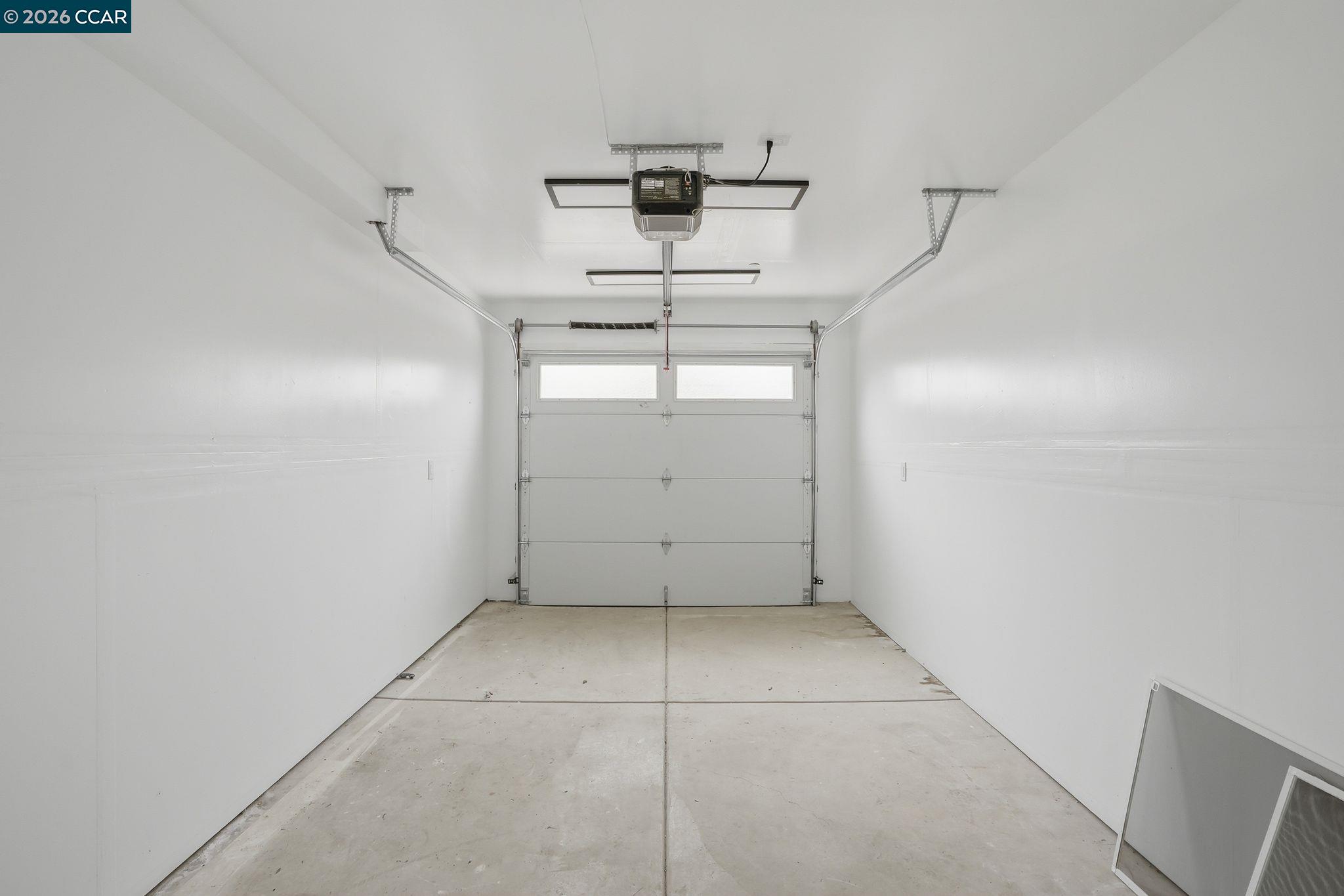 Empty garage with a concrete floor, closed windowed garage door, and ceiling-mounted opener.