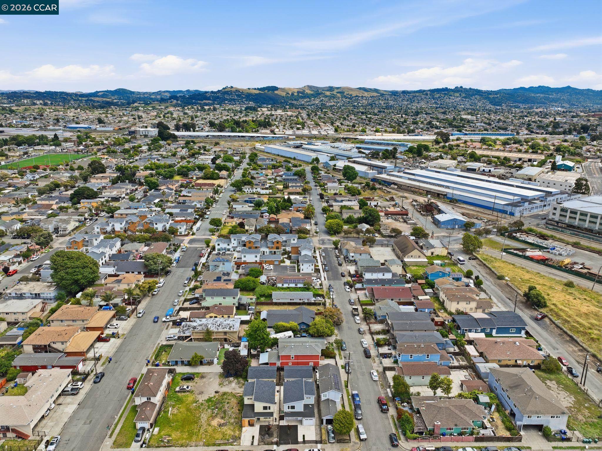 Aerial view of Richmond homes beside industrial warehouses, with rolling hills in the distance.