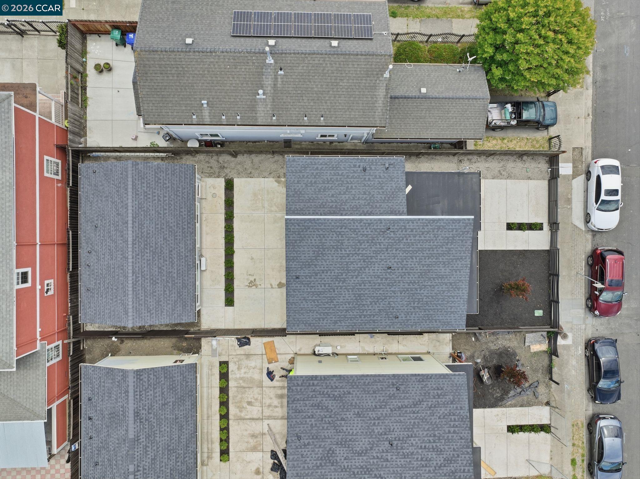 Aerial view of the residential property, with gray shingle roofs, paved walkways, and nearby parked cars.