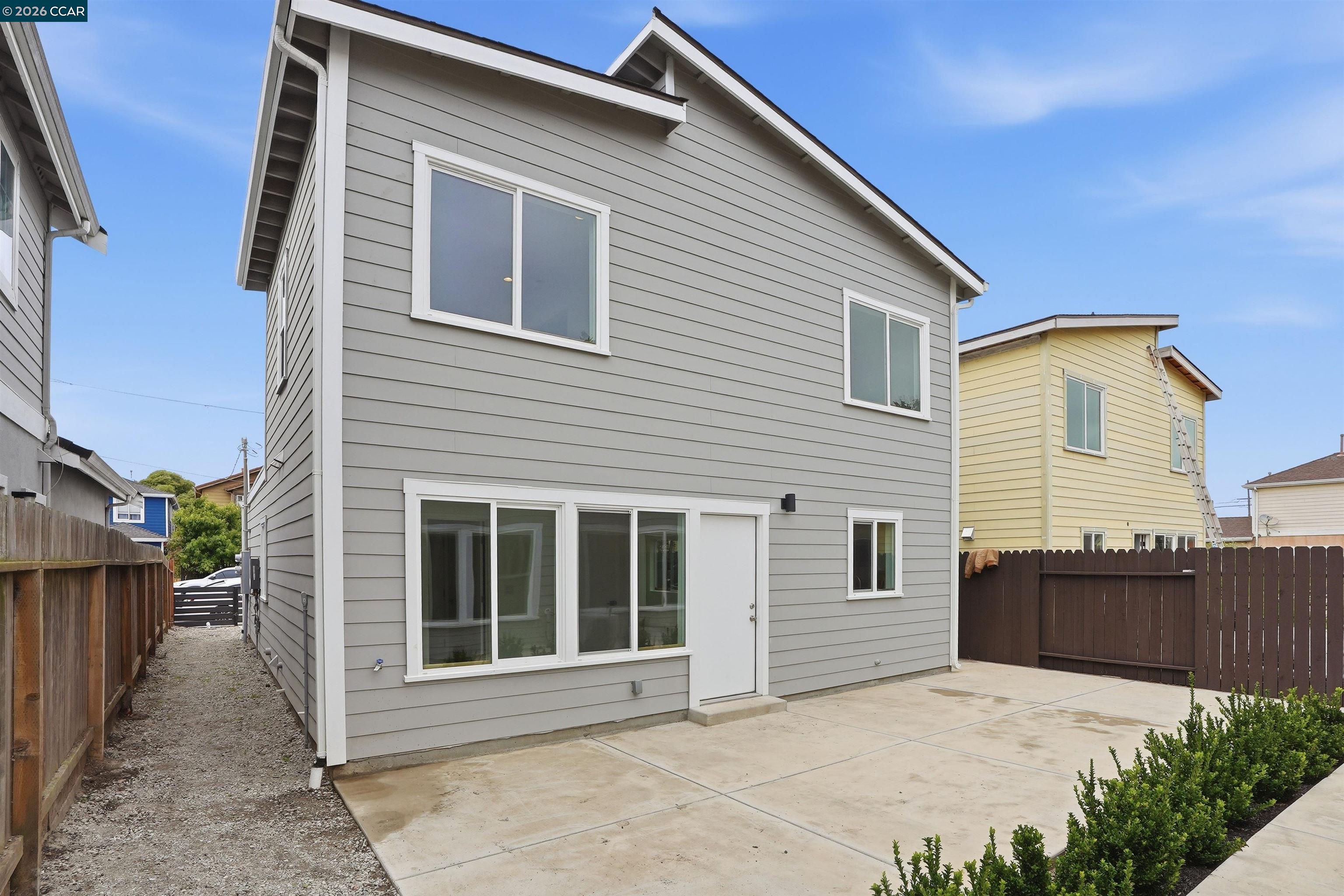 Two-story gray house with white trim, a broad concrete patio, and fenced yard.