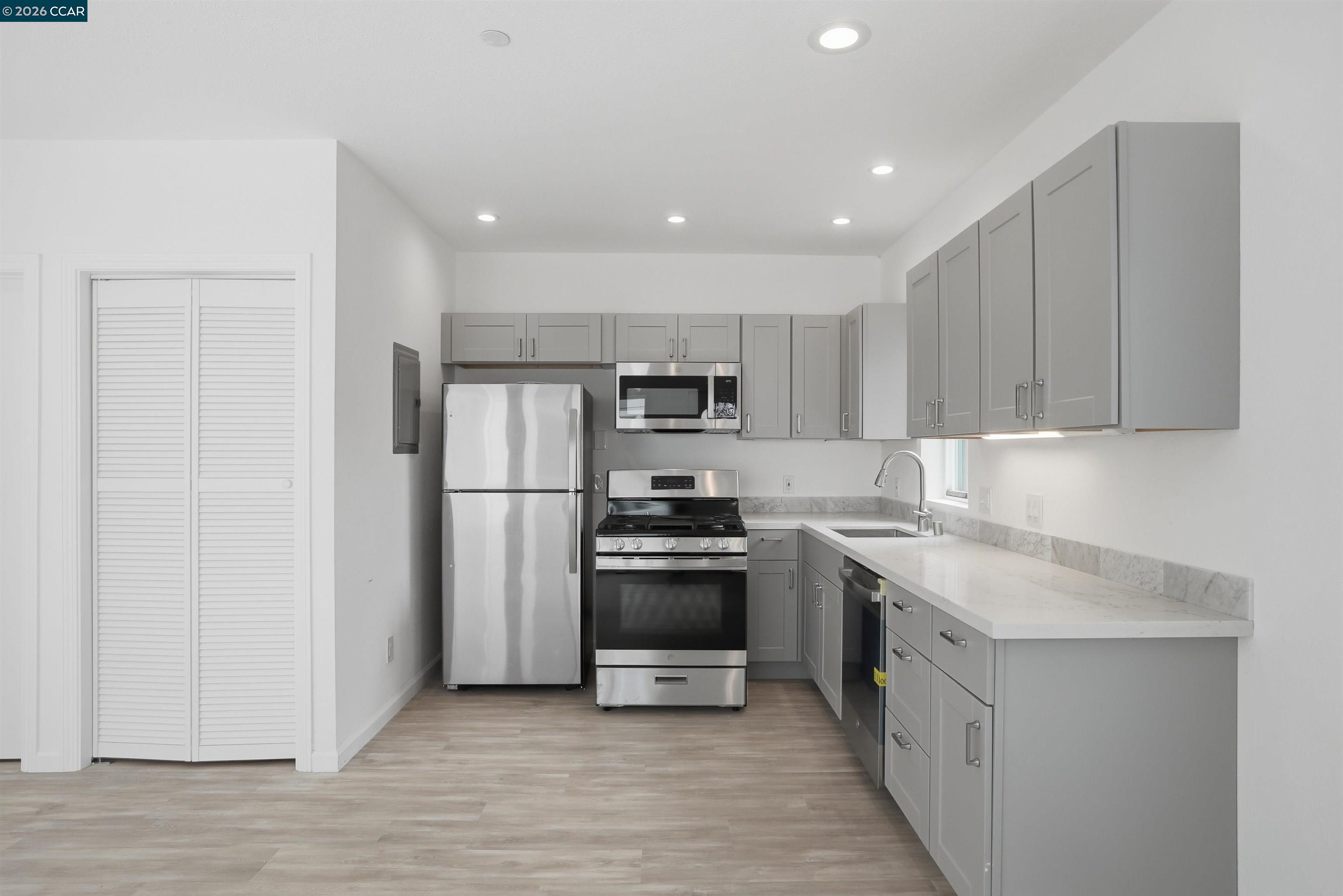 Modern kitchen with gray cabinets, stainless steel appliances, and a long white countertop.