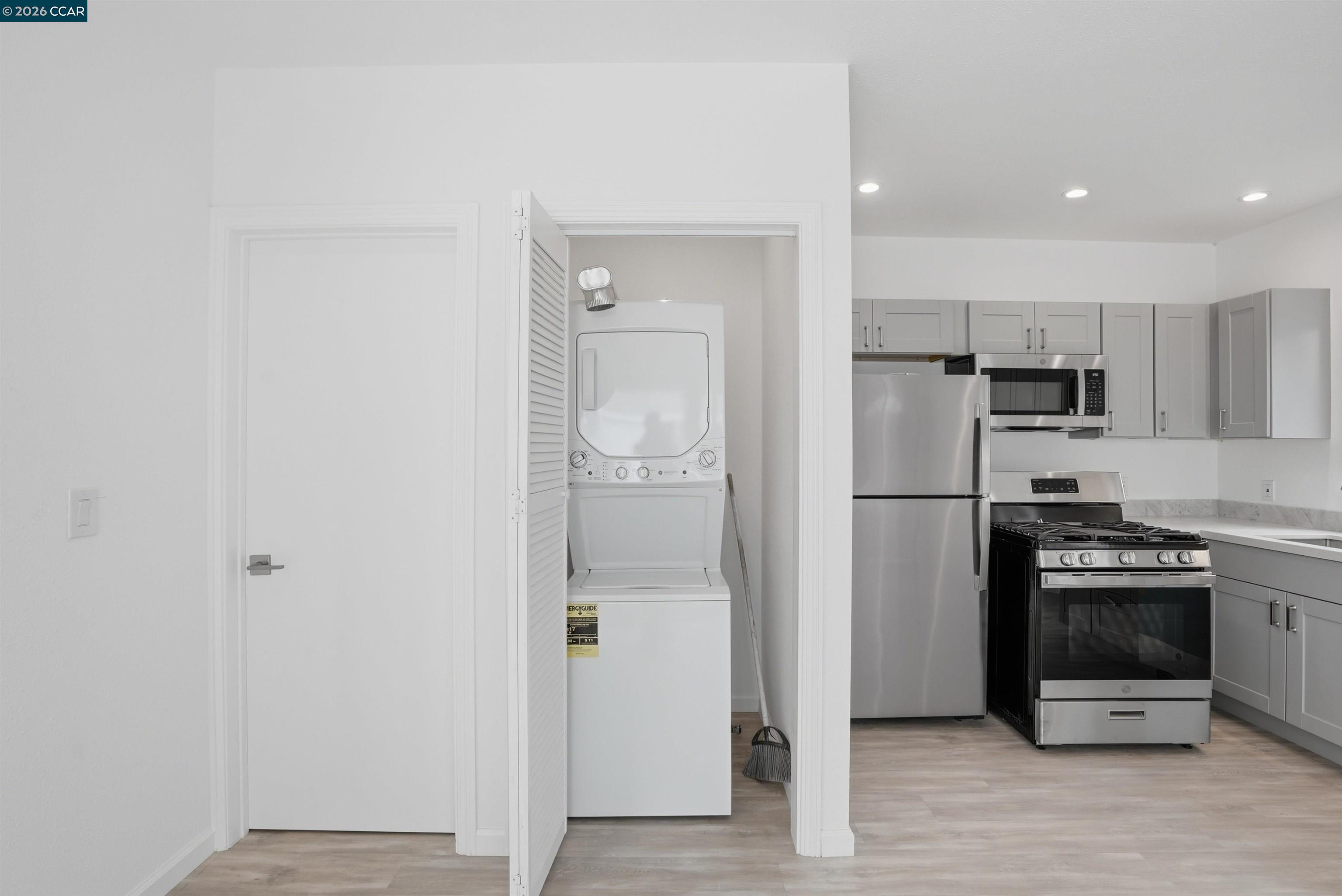 Kitchen with gray cabinets and stainless appliances beside a laundry closet with stacked washer-dryer.