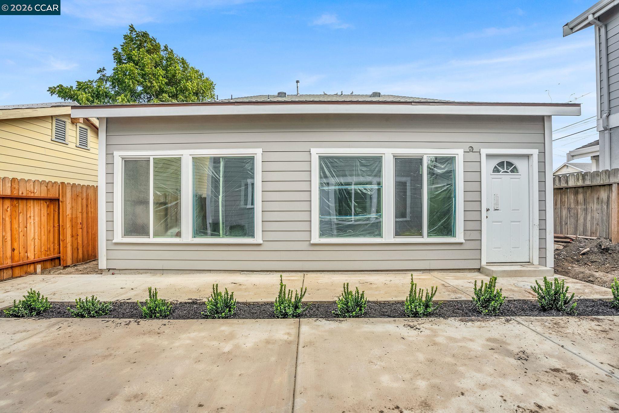 Gray single-story house with white trim, plastic-covered windows, and a concrete driveway.