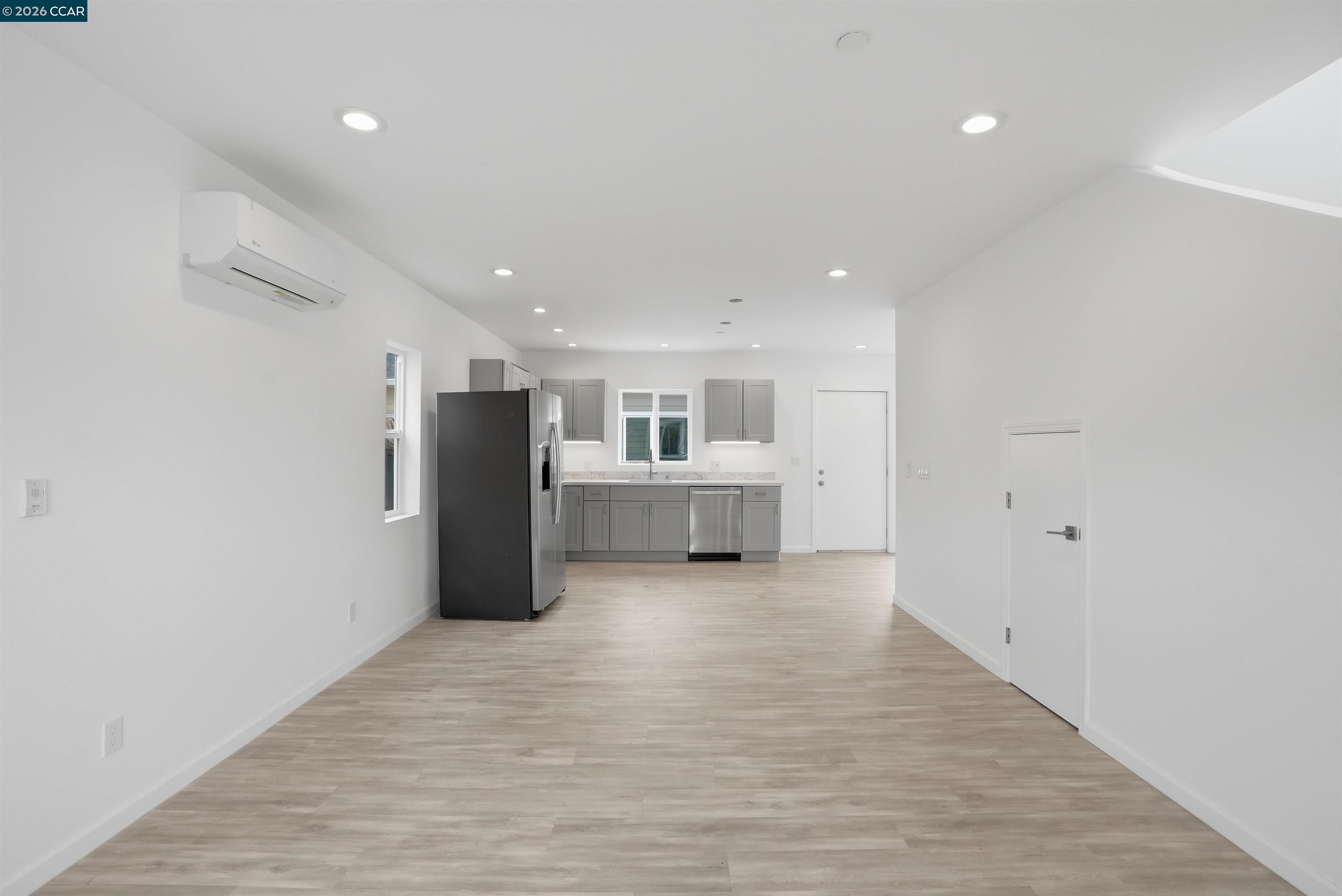 Empty open-plan kitchen with gray cabinets, stainless steel appliances, and light wood-look flooring.