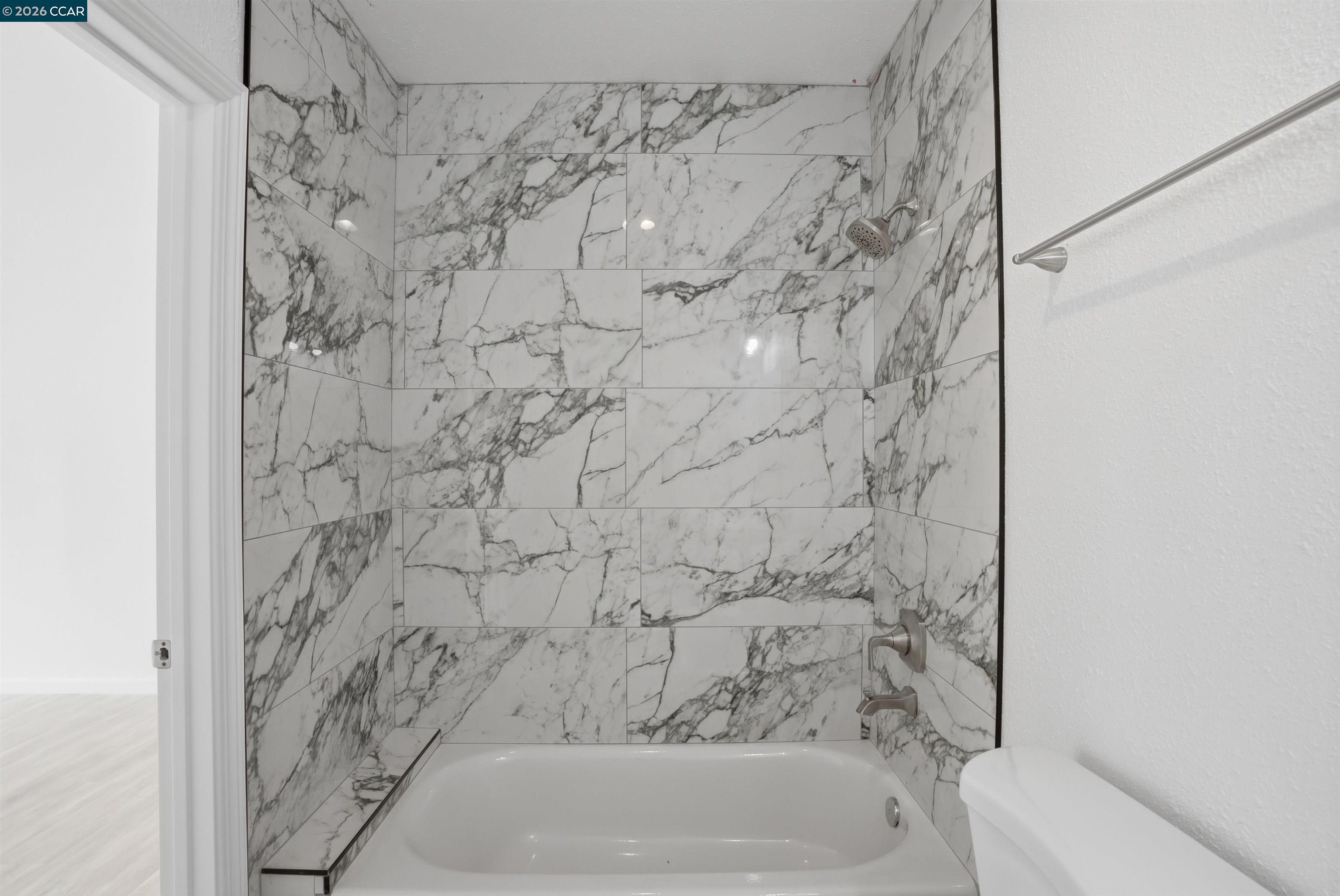 Bathroom with a white bathtub and shower featuring dramatic gray-veined tile.