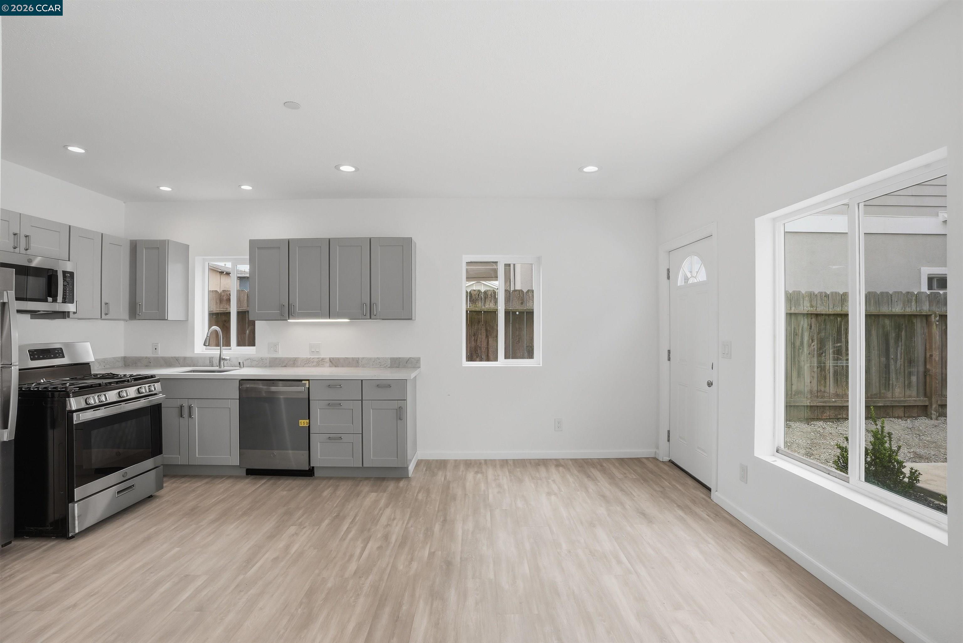 Open kitchen with gray cabinets, stainless steel appliances, and a large unfurnished dining area.