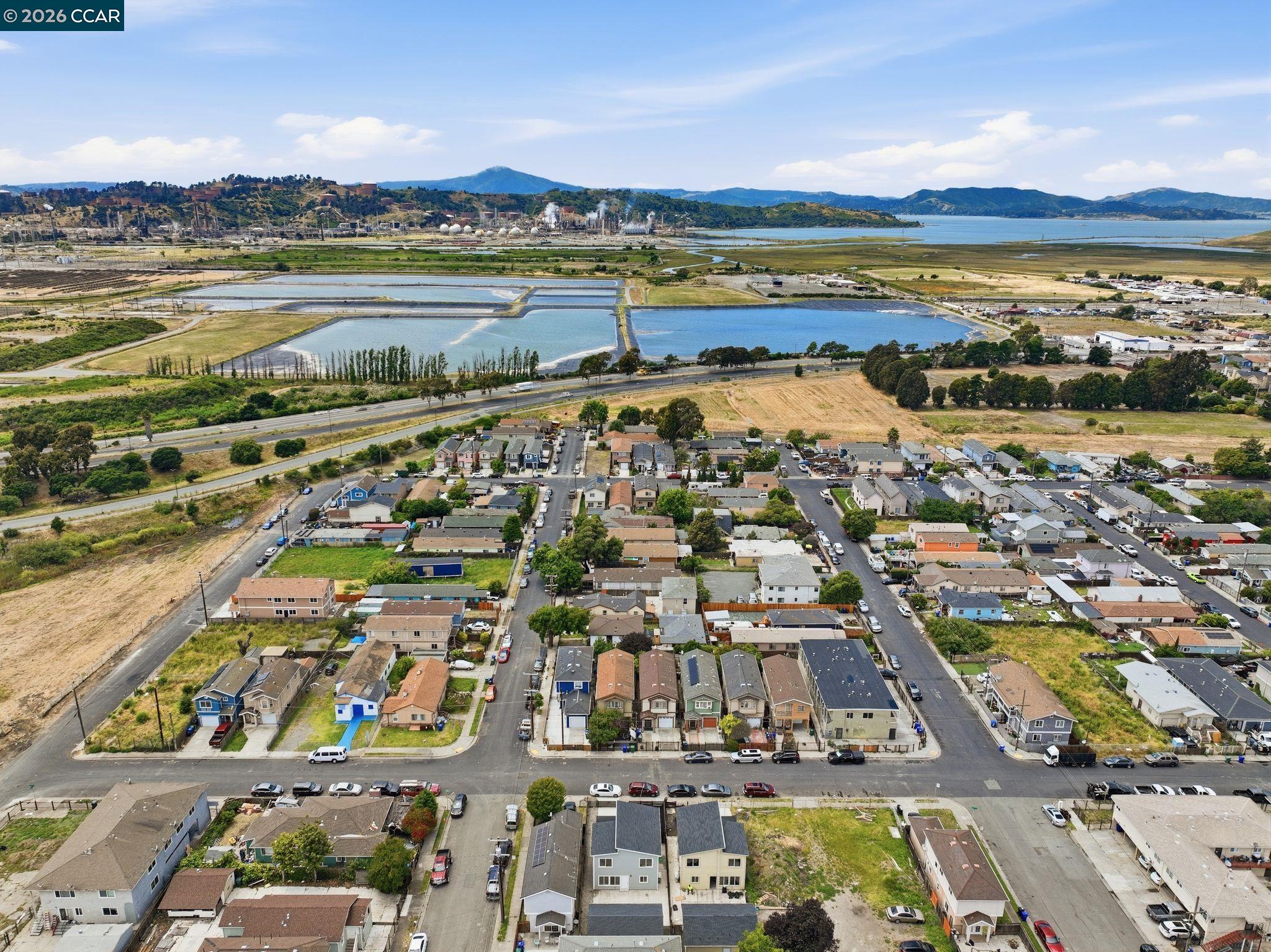 Aerial view of neighborhood homes beside wetlands, with bay and hills in the distance.