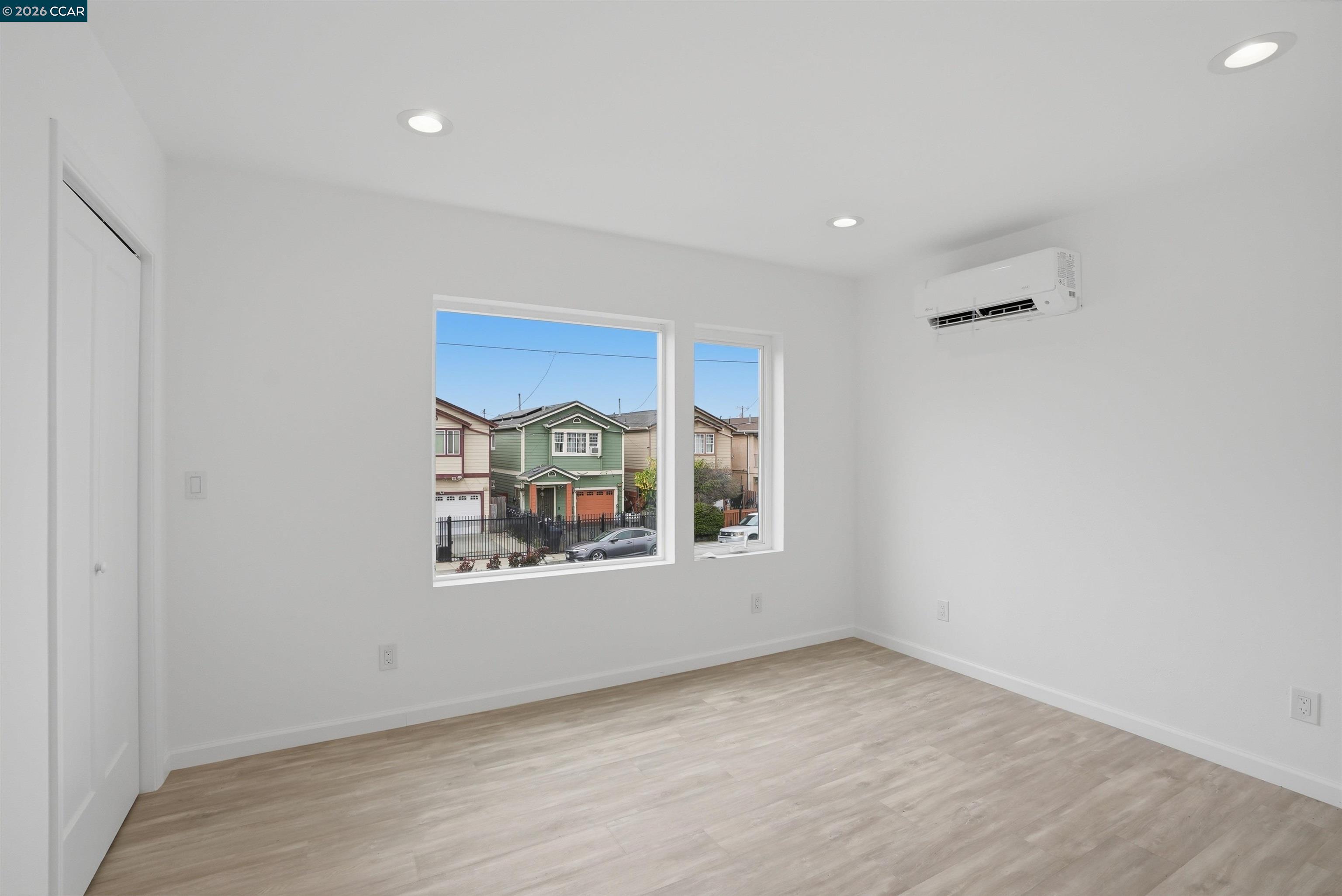 Empty bright room with light wood-look floors, two windows, and a wall-mounted mini-split.
