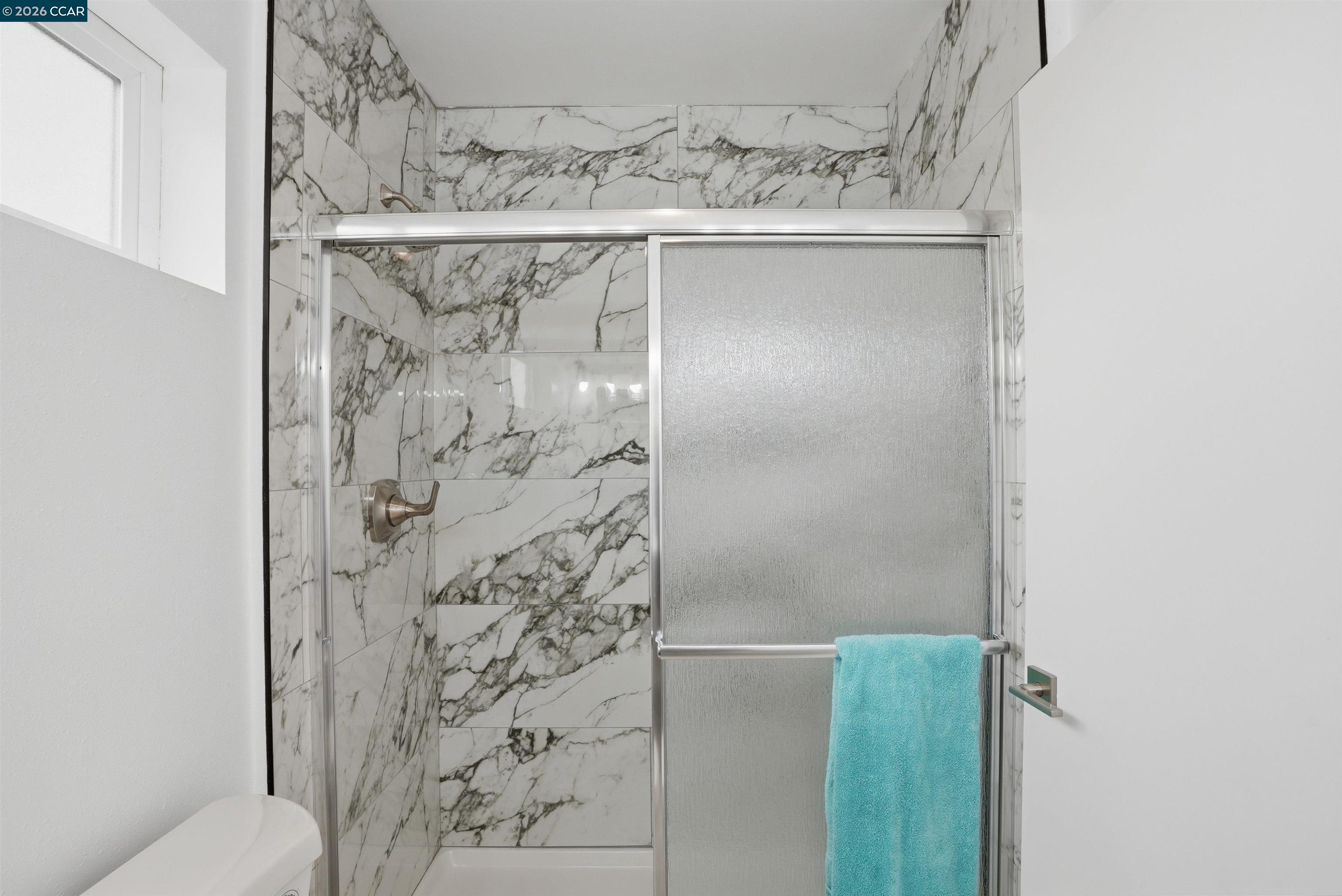 Bathroom shower with marble-look tile, a frosted-glass sliding door, and a turquoise towel.