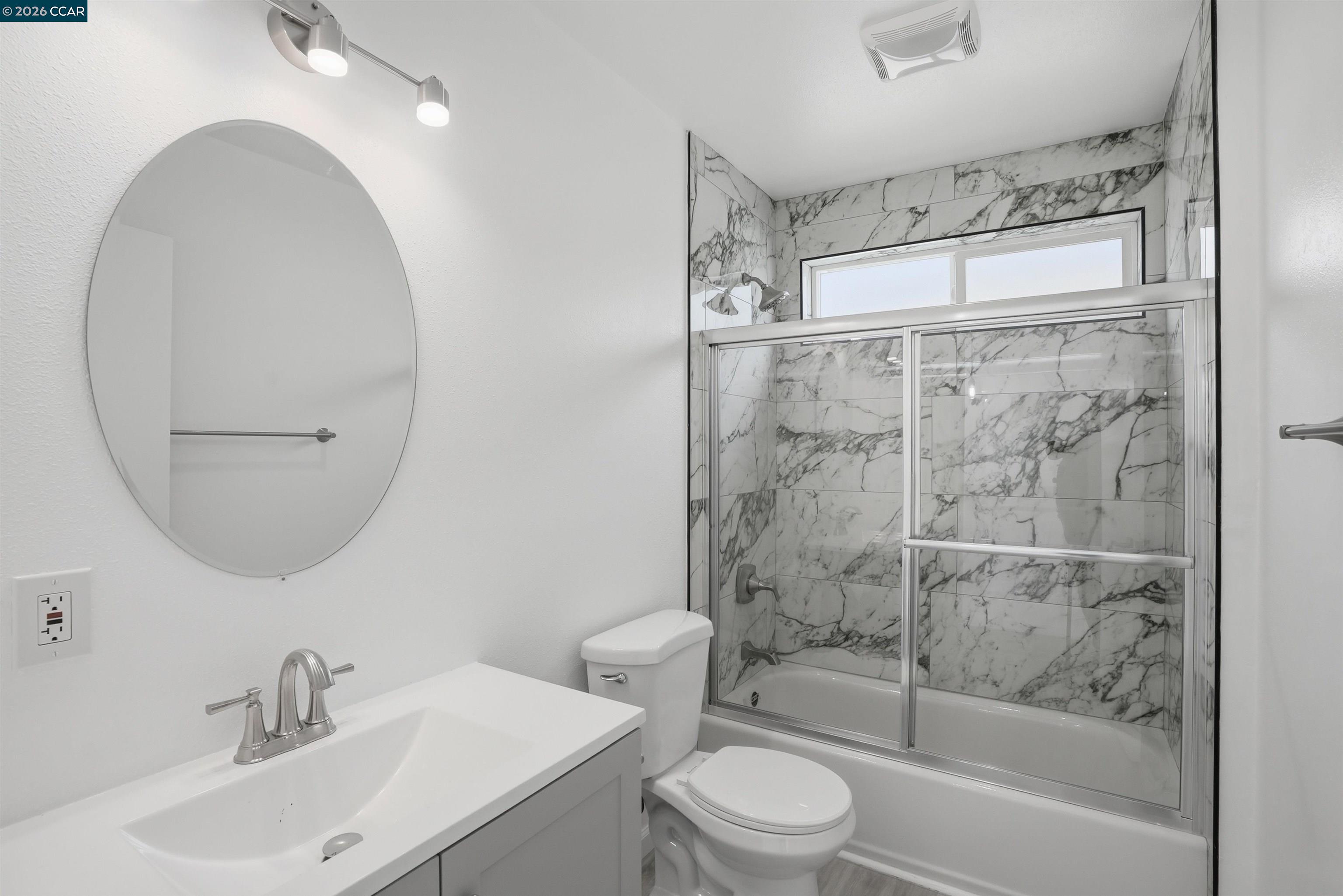 Bathroom with a glass-enclosed tub and marble-look tile shower surround.