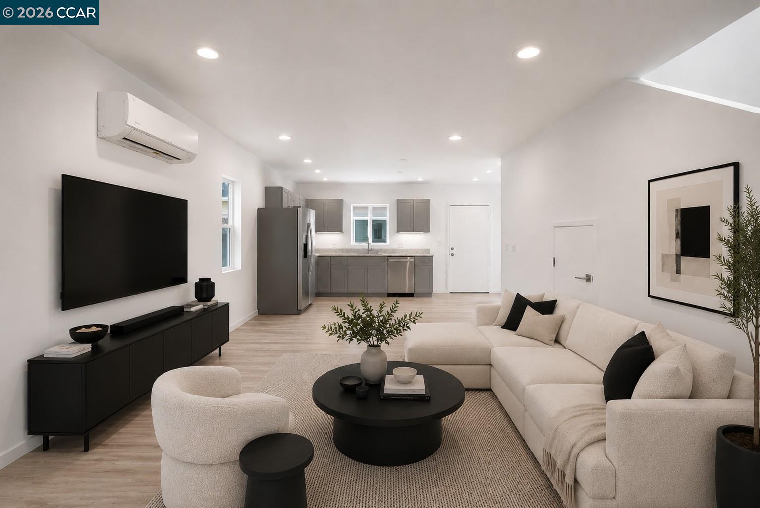 Staged living room with a cream sectional and round coffee table opening onto a gray-cabinet kitchen.