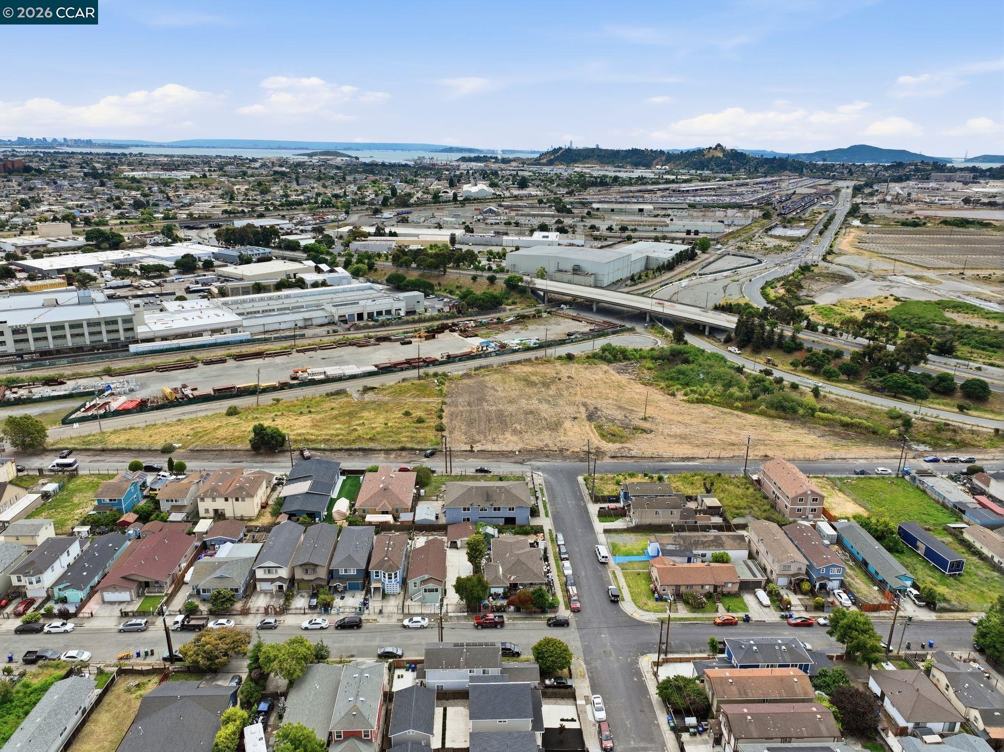 Aerial view of Richmond homes and an open lot, with industrial yards and the bay in the distance.