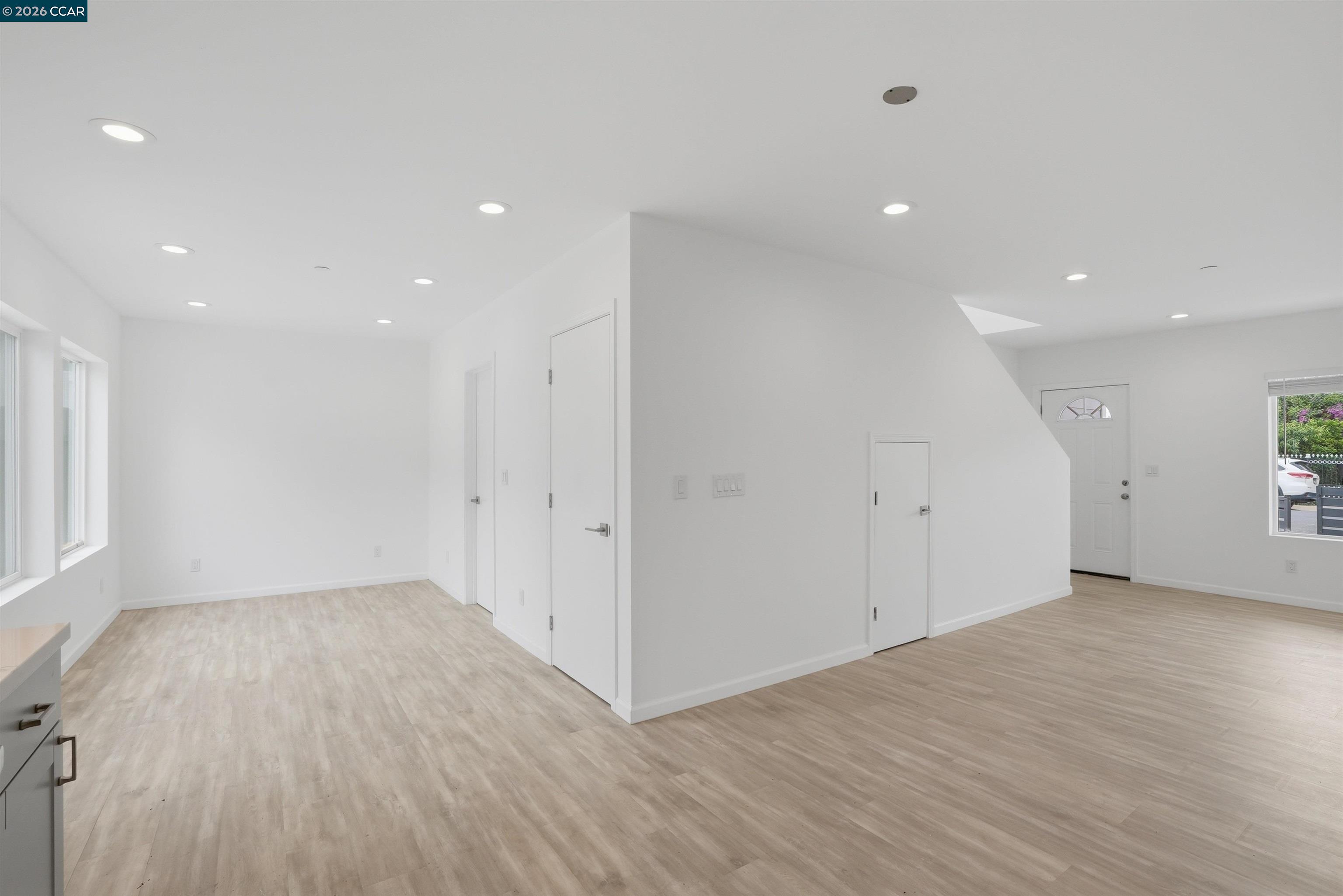 Vacant living area with light wood-look flooring, recessed lights, and windows along one wall.