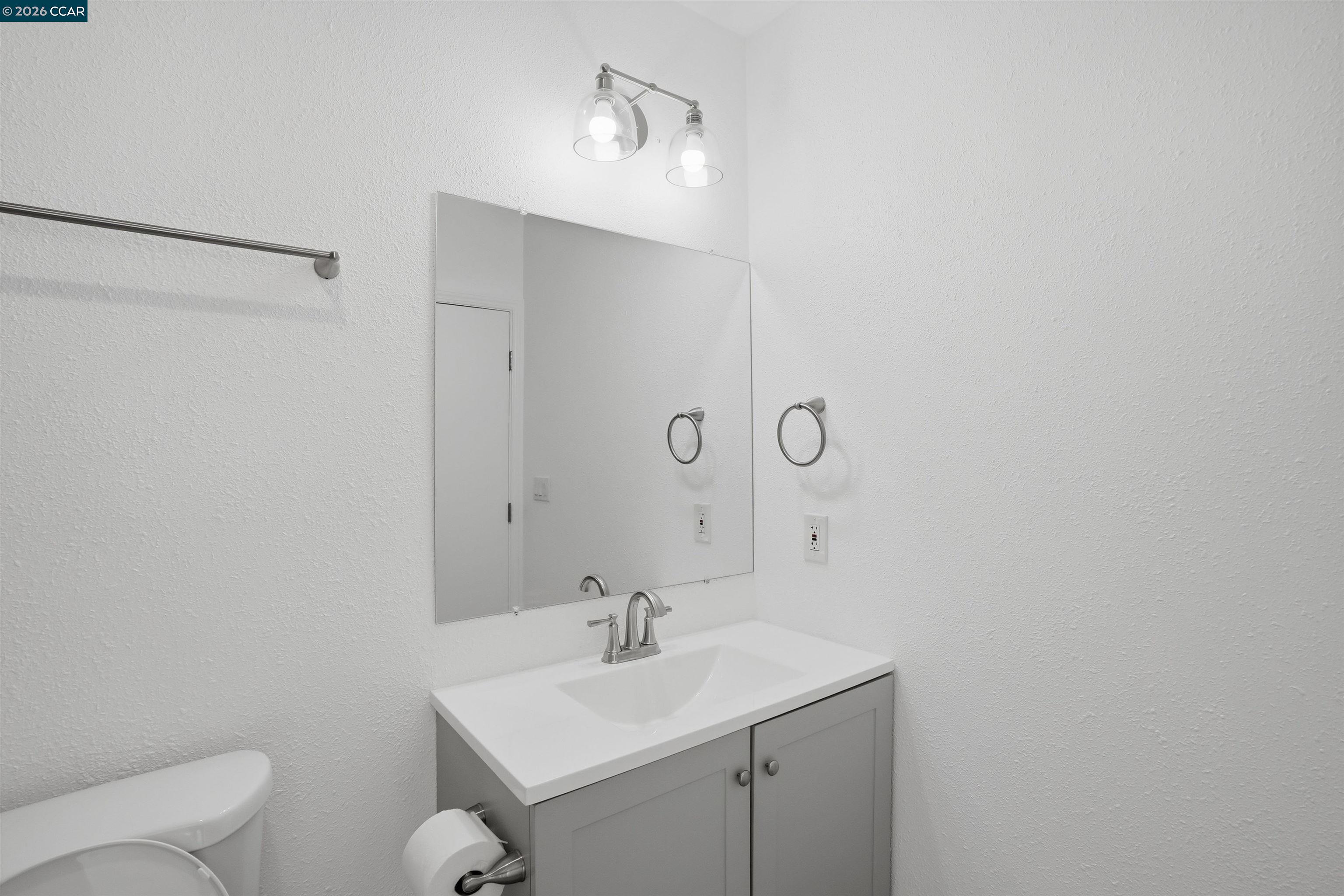 Bathroom with a white vanity, large mirror, two-light fixture, and part of a toilet.