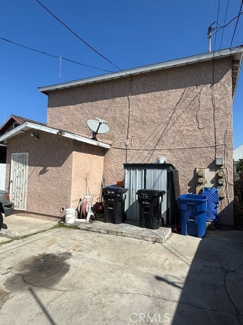 Rear exterior of a pink stucco building with utility meters and trash bins beside a concrete driveway.