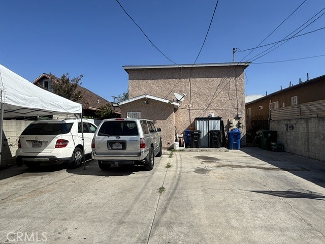 Rear exterior of a two-story stucco building with a concrete parking area and parked vehicles.