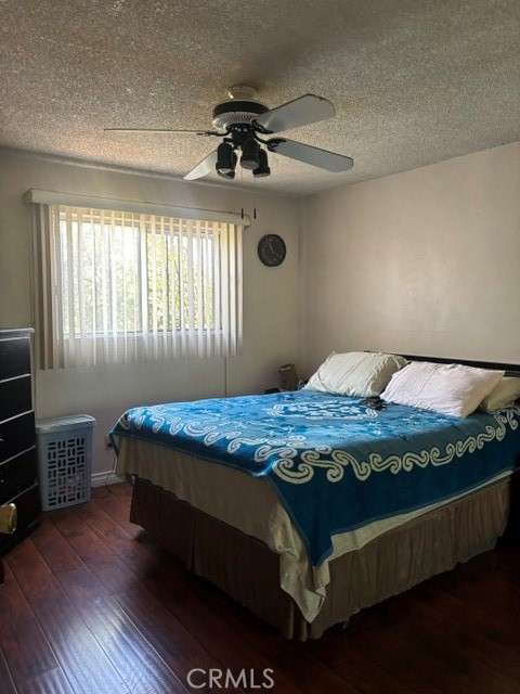 Bedroom with a blue patterned bedspread, vertical blinds, and a ceiling fan.