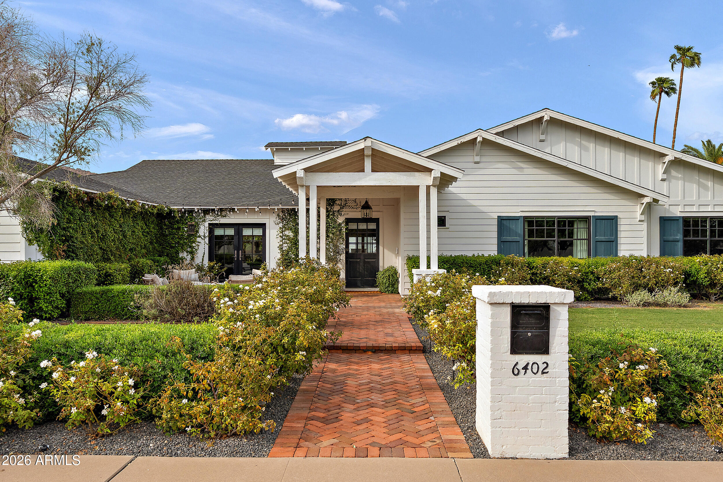 White house with blue-green shutters, landscaped garden, brick walkway, and mailbox marked 6402.