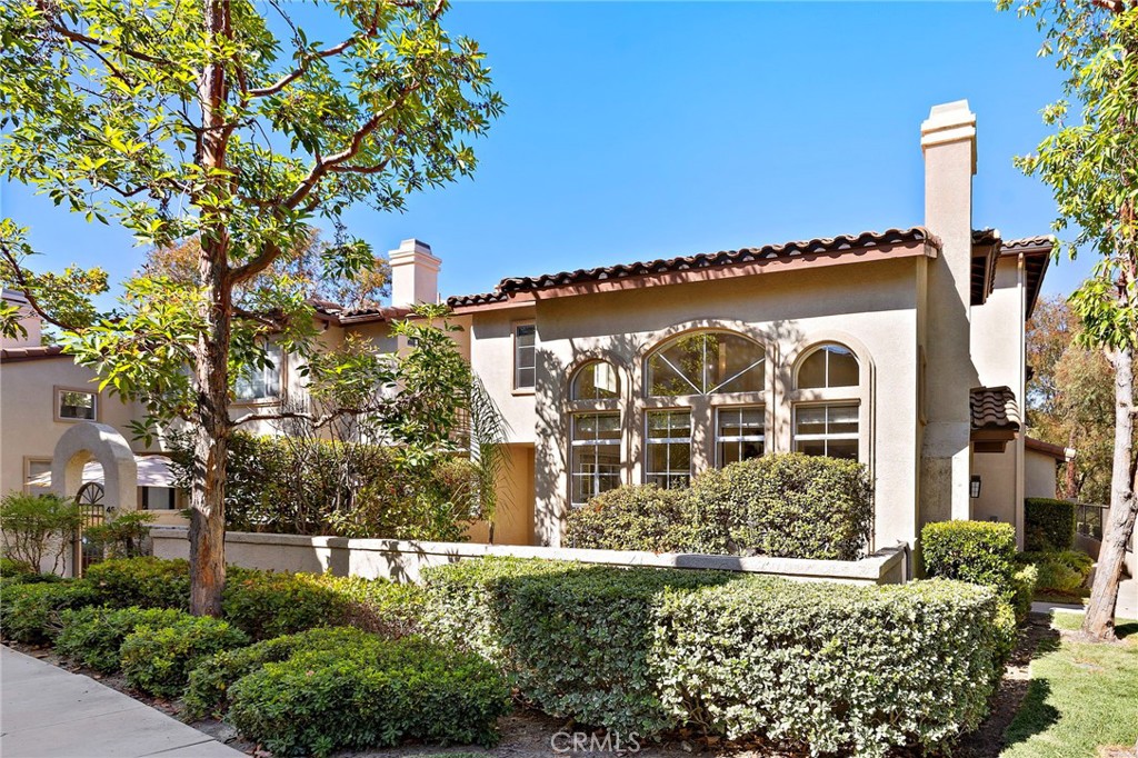 Two-story stucco home with arched windows, tile roof, and landscaped hedges.