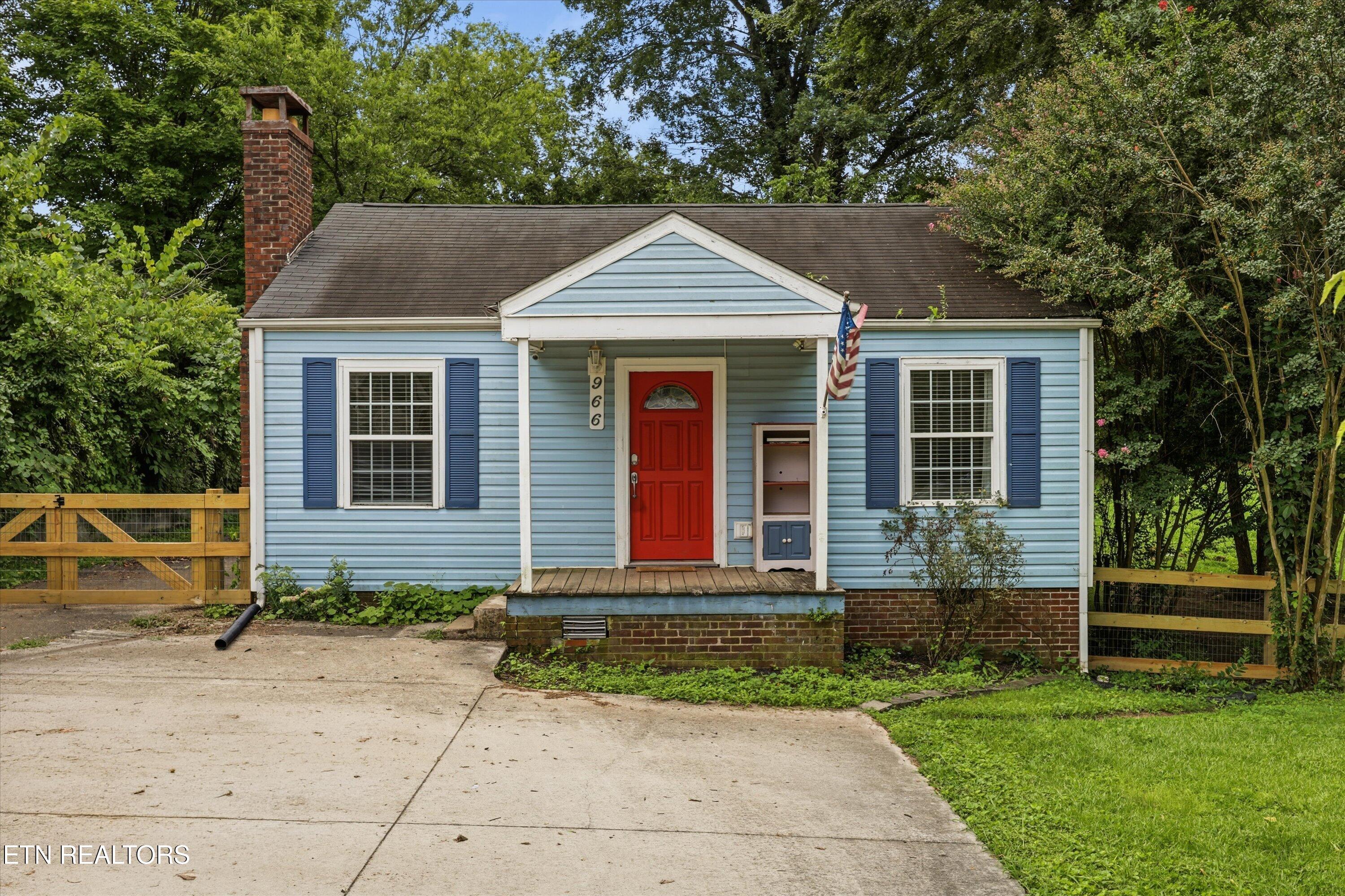 Light-blue house with a red front door, covered porch, and American flag.
