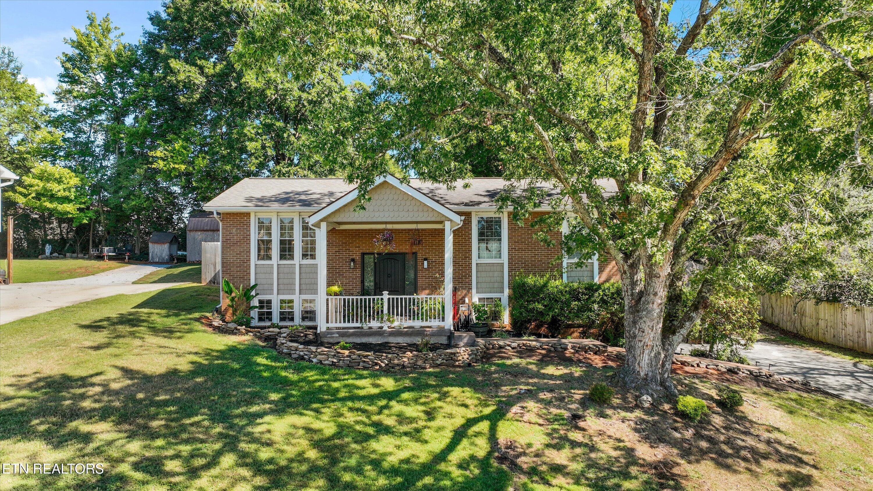 Brick home with a white covered porch beneath large shade trees and a broad front lawn.