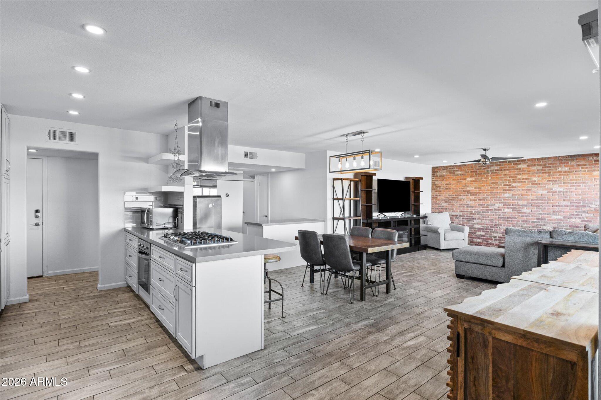 Open-plan kitchen and living room with a large island, exposed brick wall, and gray seating.